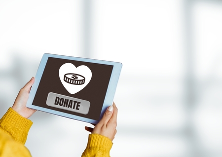 Digital composite of Hands holding tablet with Donate button and heart and money icon for charityの写真素材