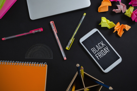Laptop, mobile phone and stationery on black background against black friday advertの写真素材