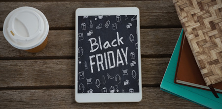 Disposable glass, books and digital tablet on wooden plank against black friday advertの写真素材