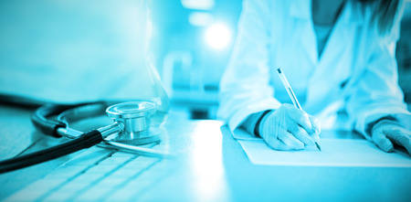 Close-up of keyboard with stethoscope against doctor writing on a paperの写真素材
