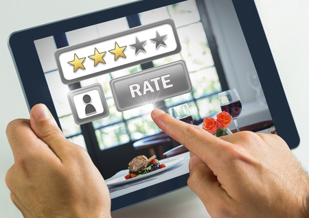 Digital composite of Hand touching tablet with Rate button and review stars in restaurant with dinner foodの写真素材