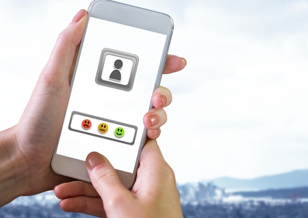 Digital composite of Hand holding phone and Feedback smiley satisfaction iconsの写真素材