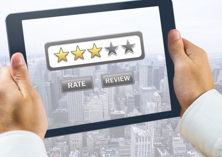 Digital composite of Hand holding tablet over city with star ratings and review buttonの写真素材