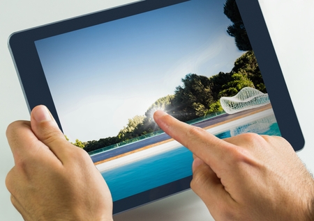Digital composite of Hand touching tablet with swimming pool
