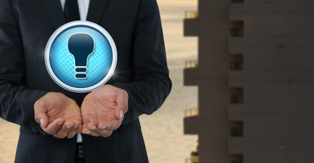 Digital composite of light bulb icon and businessman with hands palmの写真素材