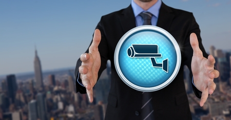 Digital composite of Security camera icon and Businessman with hands palm open in city