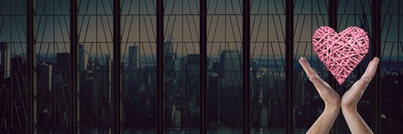 Digital composite of open hands and heart by city windowの写真素材