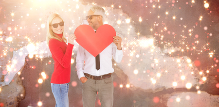 Cool couple holding a red heart together against blurred red lightの写真素材