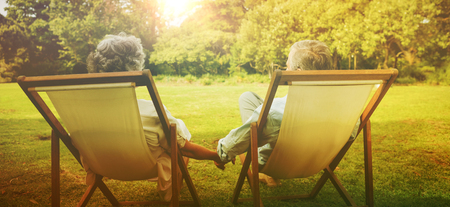 Happy mature couple sitting in park and holding handsの写真素材