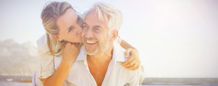 Man giving his smiling wife a piggy back at the beach on a sunny dayの写真素材