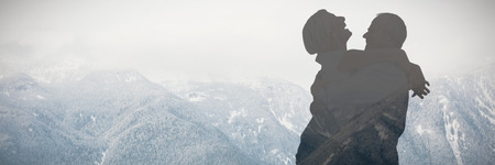 Mature couple hugging and having fun against beautiful mountain range in ski resortの写真素材