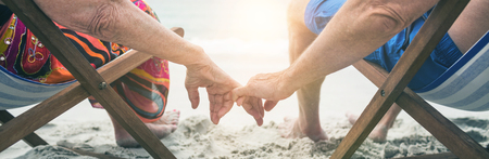 Rear view of senior couple sitting on deckchairs and holding hands while relaxing on the beachの写真素材