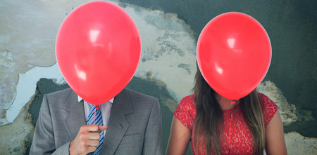 Geeky couple holding balloons in front of their faces  against rusty weathered wallの写真素材