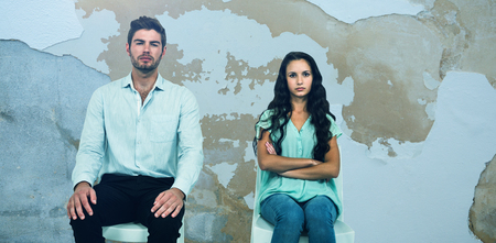 Couple sitting on chairs not talking after argument against rusty weathered wall