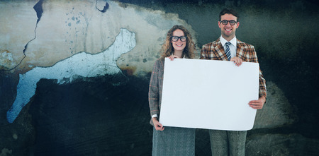 Geeky hipster couple holding poster against rusty weathered wallの写真素材