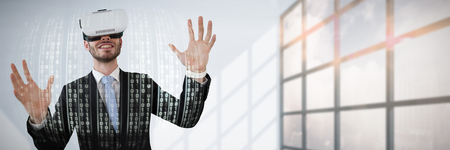 Smiling businessman with vr glasses gesturing against white background against interior of empty roomの写真素材