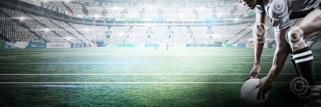 Rugby player holding ball while bending against stadium against skyの写真素材