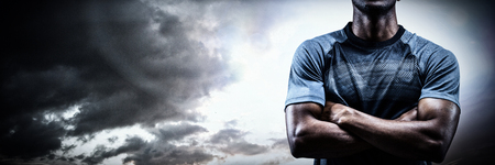 Thoughtful athlete standing with arms crossed against spotlight in skyの写真素材