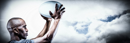 Athlete in position of throwing rugby ball against spotlight in skyの写真素材
