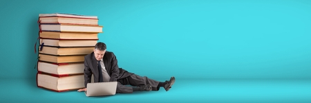 Digital composite of Business man using computer on the floor next to a pile of books on blue backgroundの写真素材