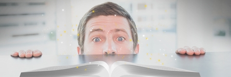 Digital composite of Man looking at an opened book with lights on a tableの写真素材