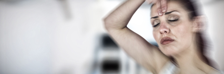 Beautiful woman with eyes closed white touching forehead against operating room with surgical equipment in hospitalの写真素材