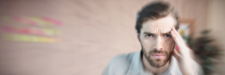 Portrait of man suffering from headache against close-up of office deskの写真素材