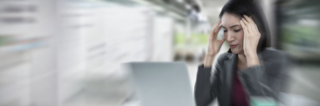 Businesswoman with laptop suffering from headache against digital image of corridor in modern office