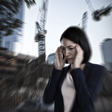 Businesswoman suffering from headache against low angle view of cranes by buildingsの写真素材