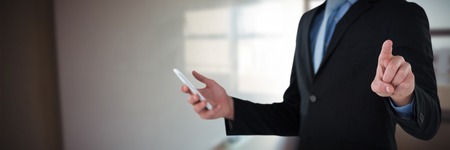 Mid section of businessman holding mobile phone while using interface screen against whiteboard in meeting roomの写真素材