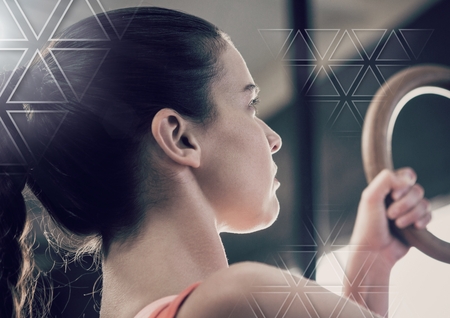 Digital composite of athletic fit woman in gym using rings with triangle interfaceの写真素材