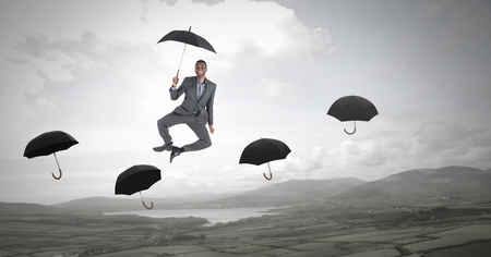 Digital composite of man holding umbrella jumping across umbrellas over nature landscapeの写真素材