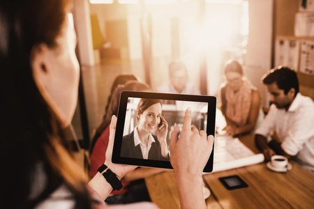 Businesswoman using digital tablet while discussing with colleagues against smiling businesswoman talking on mobile phone in office corridorの写真素材