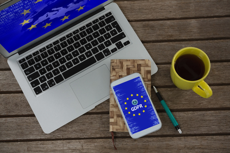 Laptop, mobile phone, dairy, pen and coffee on wooden plank against european union locked
