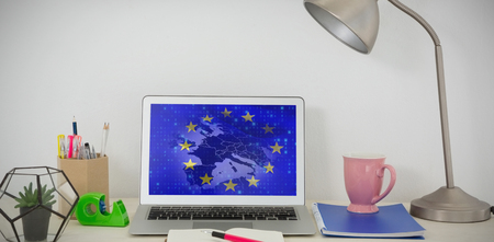Laptop and various office accessories on table against european union flag with binary codesの写真素材