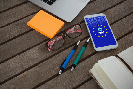 Mobile phone, laptop, pen, sticky note, spectacles and organizer on wooden plank against european union lockedの写真素材