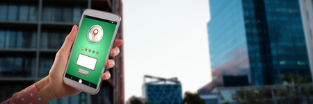 Womans hand showing mobile phone against view of residential buildingsの写真素材