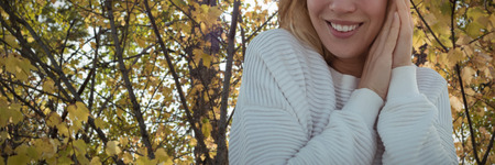 Portrait of smiling woman wearing sweater with hands clasped against branch of maple leaves in...