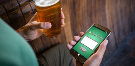 Satisfaction against cropped hands of man using phone while having beerの写真素材