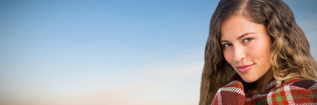 Portrait of smiling beautiful woman wrapped in blanket against beautiful sunset on a sunny dayの写真素材