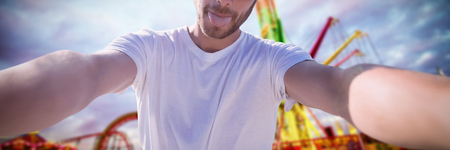 Young man taking a selfie against fairground ride in amusement parkの写真素材