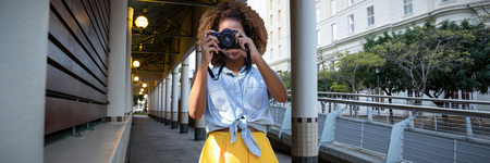 Young woman holding camera against architectural columns in buildingの写真素材