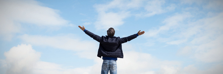 Rear view of a man raising his arms up against forest and fieldsの写真素材