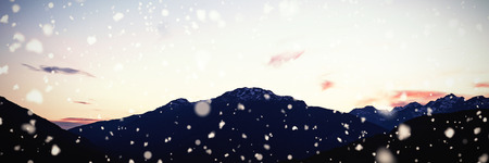 Snow falling against sun setting behind rocky mountain rangeの写真素材