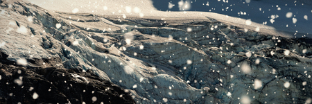 Snow falling against rock mountain covered with glacierの写真素材