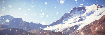 Snow falling against snow capped mountains on a sunny dayの写真素材