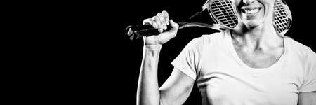 Portrait of female tennis player posing with racket on black backgroundの写真素材
