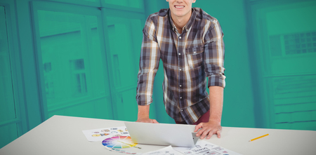 Portrait of confident businessman standing at table with laptop against modern officeの写真素材