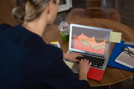 Business graph and chart against rear view of businesswoman using laptop in officeの写真素材