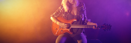 Young female guitarist performing in illuminated nightclubの写真素材